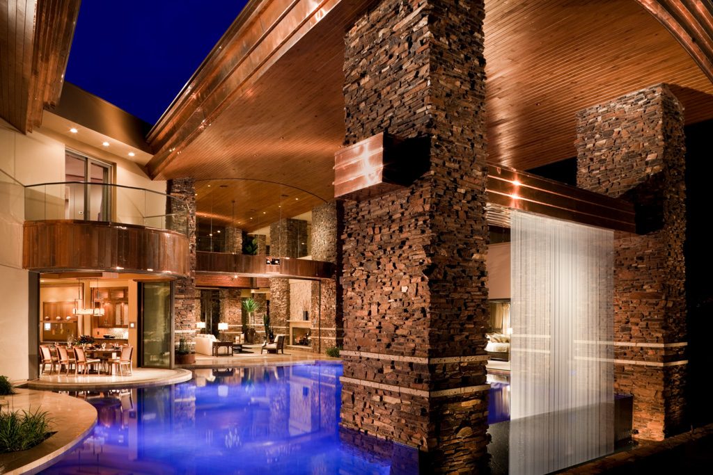 Modern stone-and-glass Las Vegas home with a glowing pool at twilight